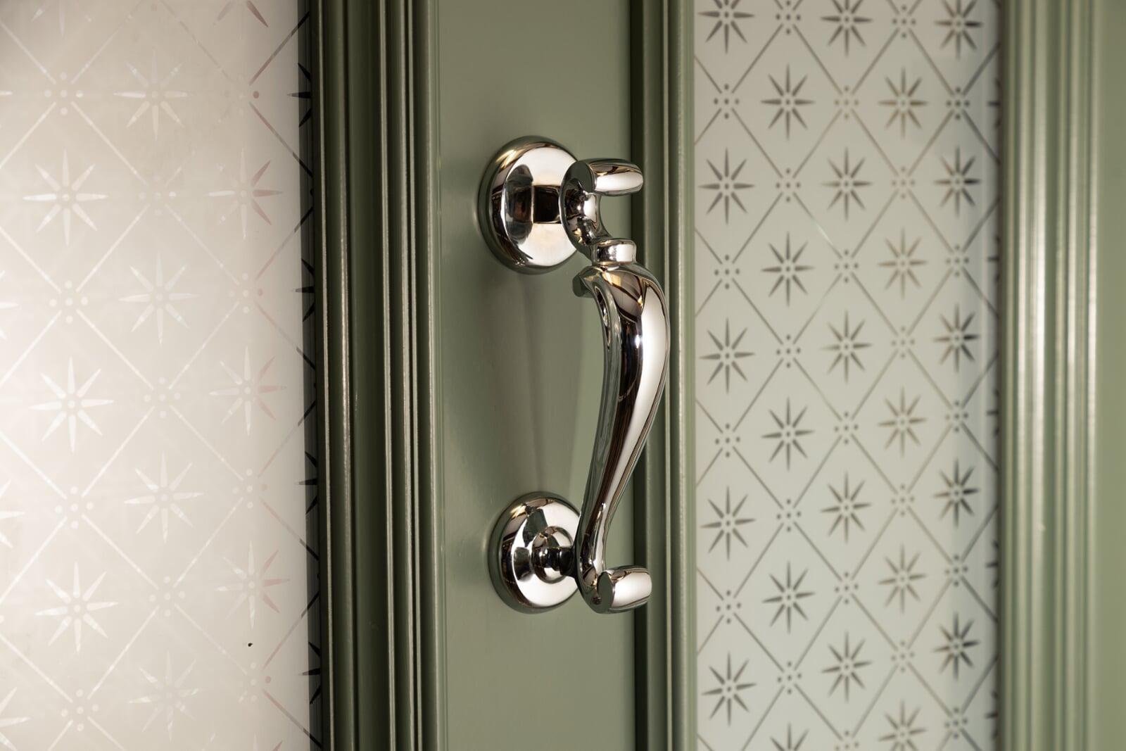 Polished door pull handle on painted timber entrance door with decorative glass panel