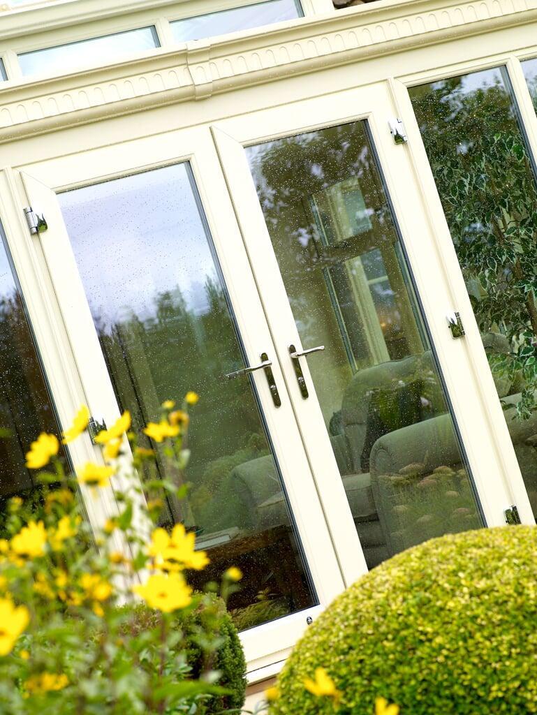 Close view of white PVC French doors with glazed panels and garden planting