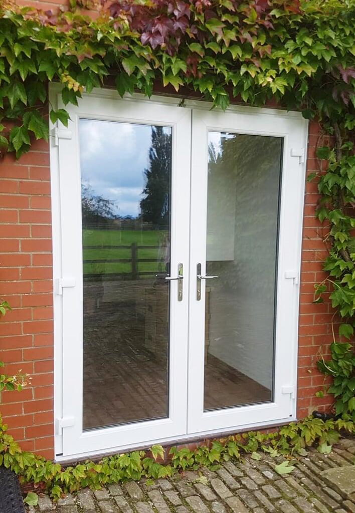 White PVC double patio doors installed in a red brick exterior wall